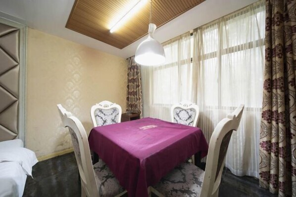 A dining area with a table covered in a purple tablecloth, four chairs with patterned upholstery, a hanging light fixture, and a window with sheer curtains. - Yongxing He'an Business Hotel (Yongxing)