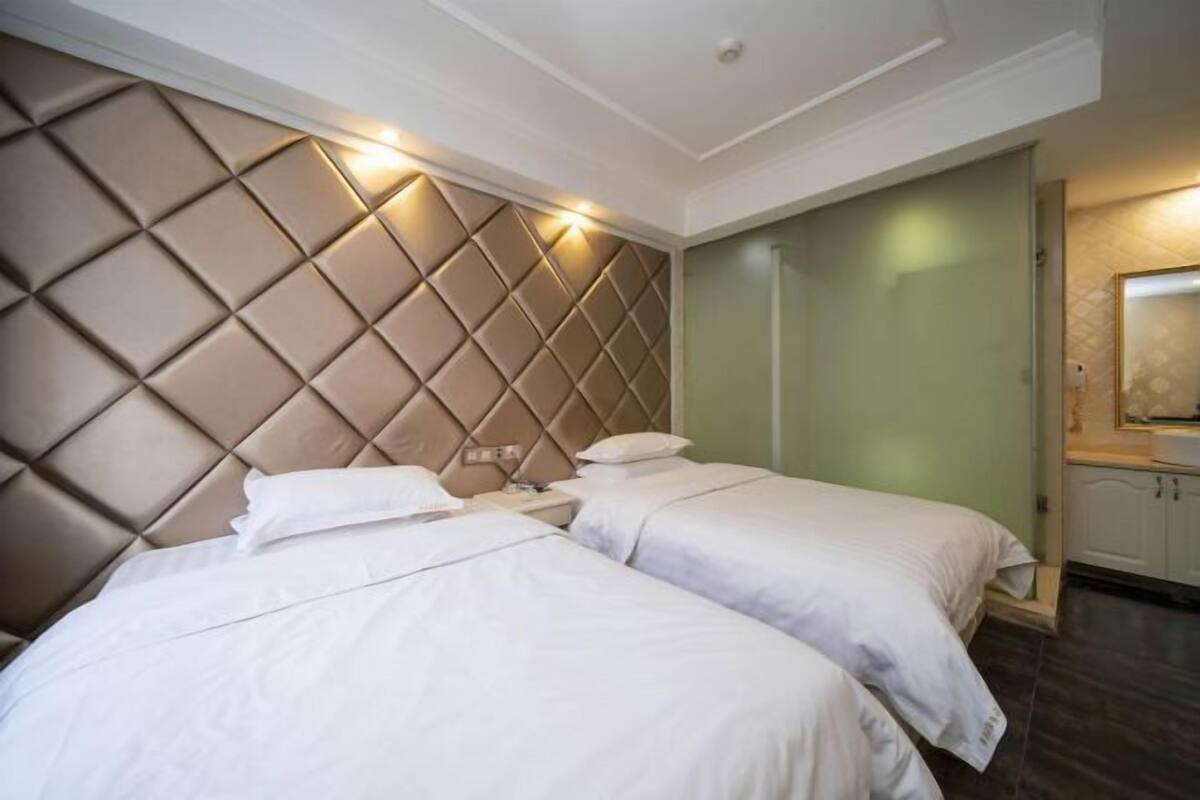 Een hotelkamer met twee bedden, een gestoffeerd hoofdbord, een groene wand en een kleine badkamer met spiegel.