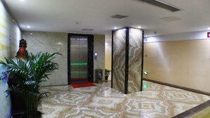 Un vestíbulo con piso de mármol, un ascensor, una estatua y una planta en maceta.