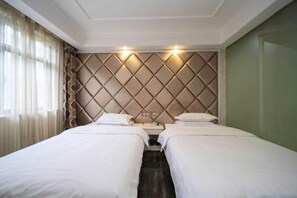Une chambre d’hôtel avec deux lits simples, une tête de lit rembourrée, une table de chevet et une fenêtre avec des rideaux.