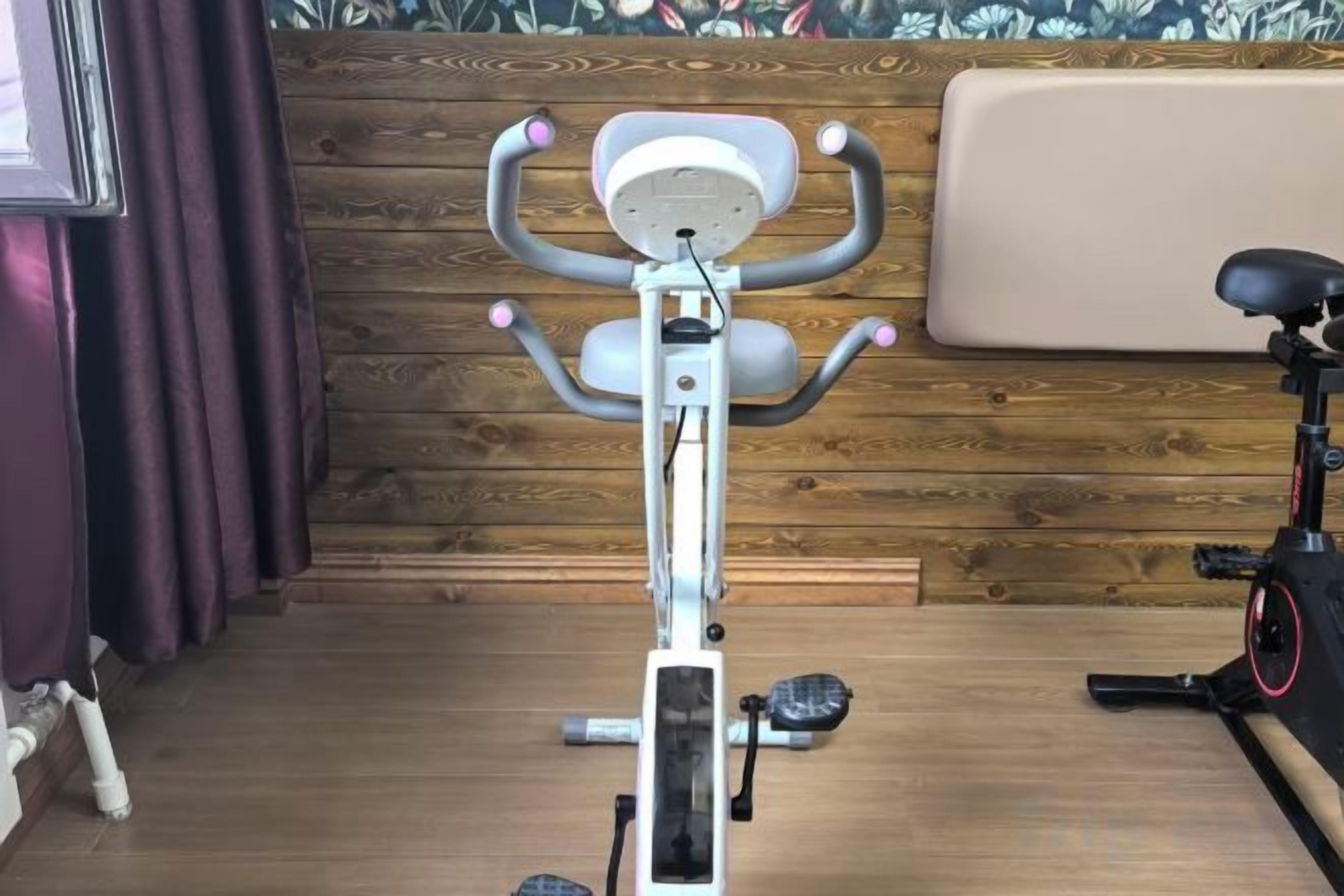A stationary exercise bike in a room with wooden paneling and a cushioned bench.