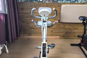 A stationary exercise bike in a room with wooden paneling and a cushioned bench. - Forest Snow Hotel (Genhe)