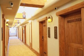 Un pasillo de hotel con puertas de madera, luminarias fijadas a la pared y piso alfombrado.