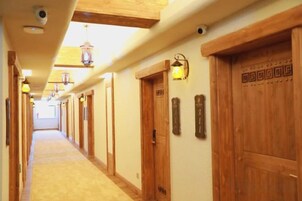 Un pasillo de hotel con puertas de madera, luminarias fijadas a la pared y piso alfombrado.