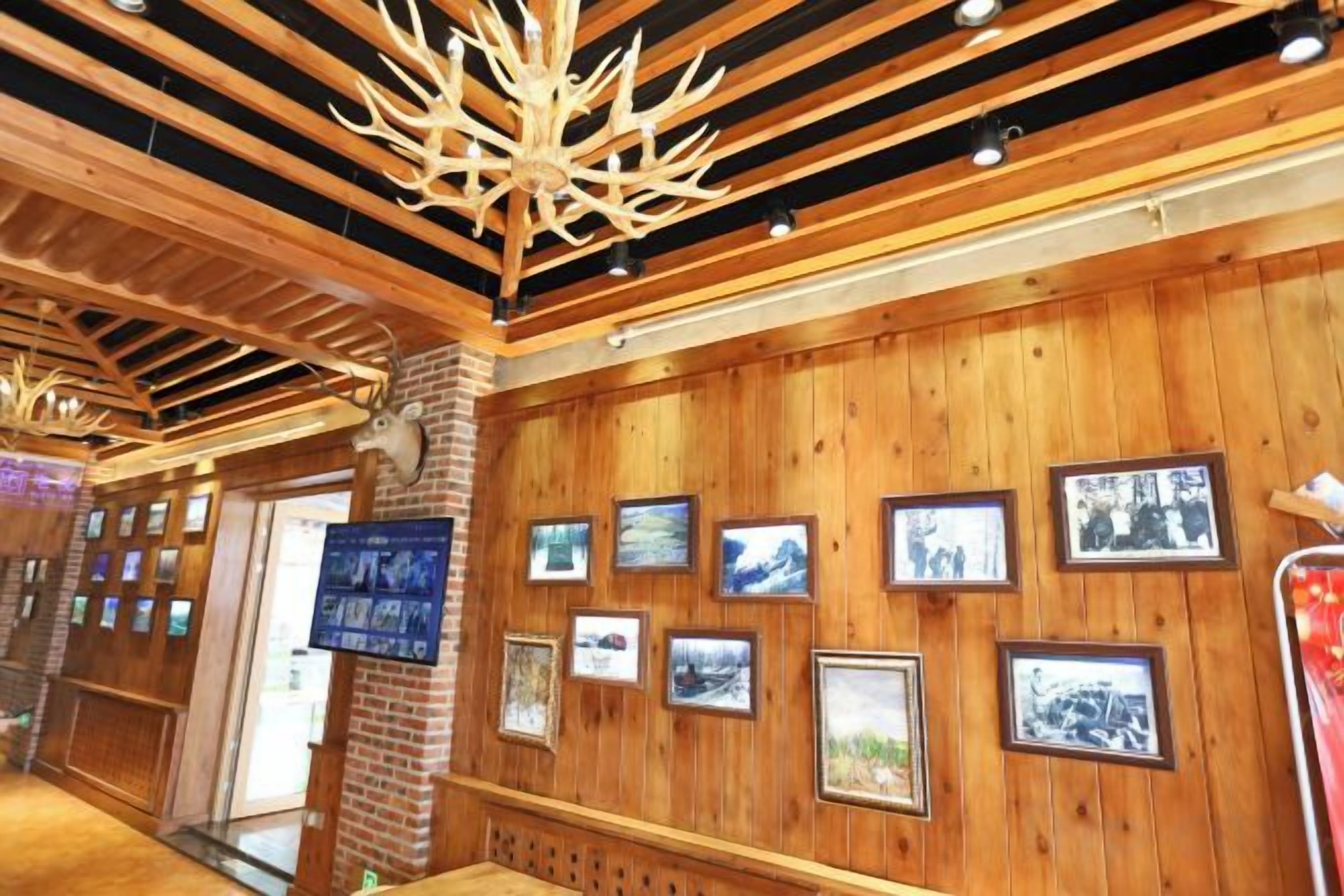 A wooden interior with framed pictures on the walls, a wooden ceiling with beams, and a brick pillar.