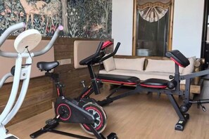 A home gym with an exercise bike, a stationary bike, and a bench. - Forest Snow Hotel (Genhe)