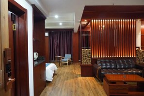 A room with a wooden floor, a sofa, a coffee table, a chair, a small table with a lamp, and a curtain. - Forest Snow Hotel (Genhe)