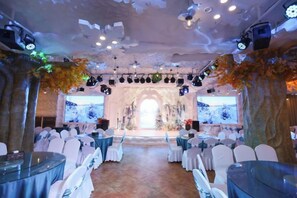 A banquet hall with round tables, chairs, and a stage with a backdrop. - Forest Snow Hotel (Genhe)