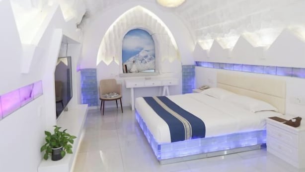 Un dormitorio moderno con cama, mesita de noche, silla y escritorio con espejo.