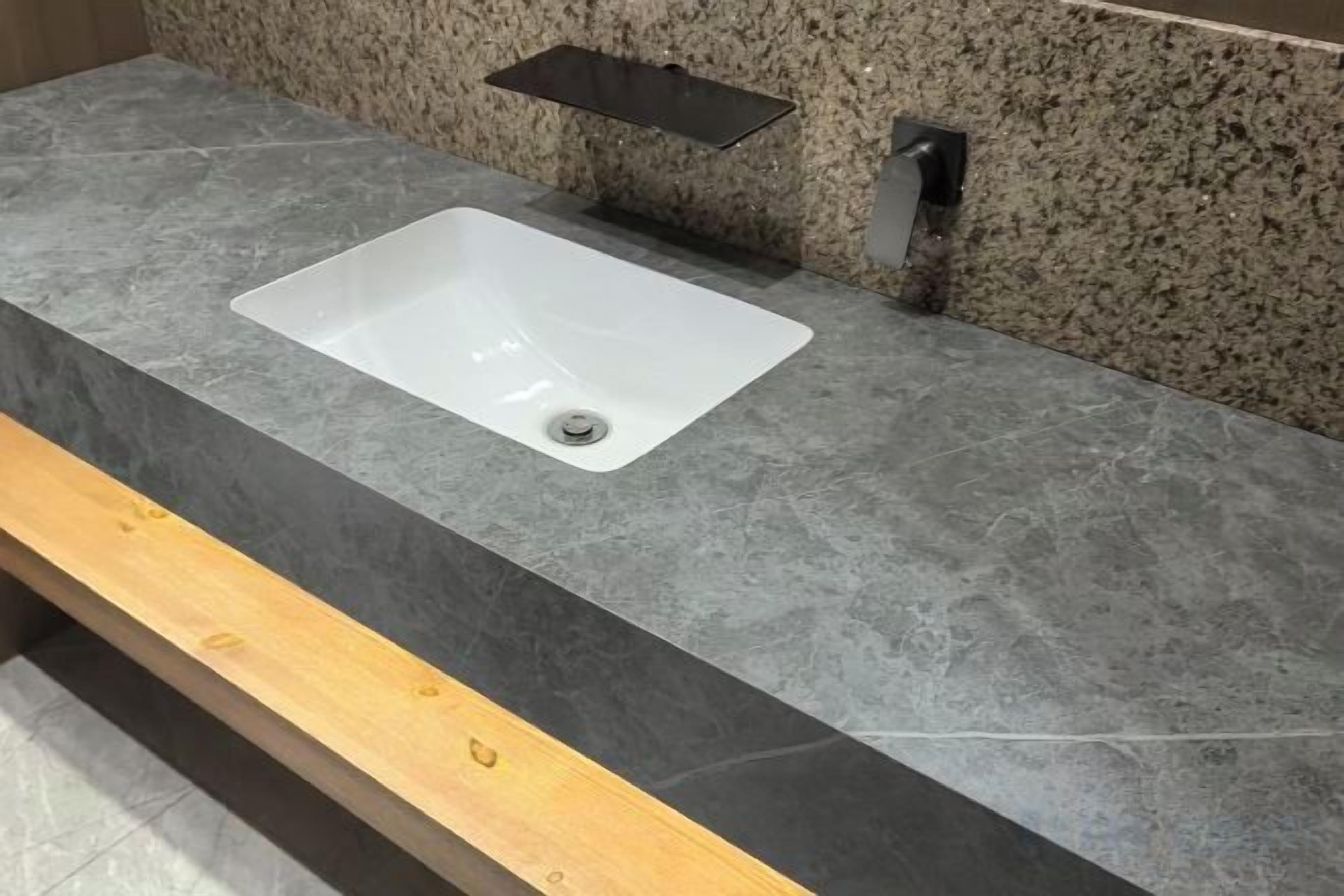 A bathroom with a white sink, granite countertop, and a wooden bench.