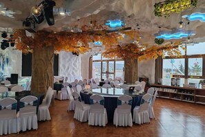 A restaurant with round tables, white chairs, and a view through large windows. - Forest Snow Hotel (Genhe)
