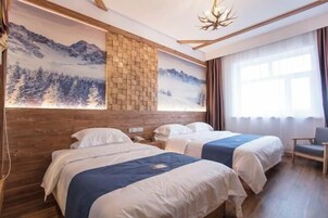 Habitación de hotel con dos camas, cabecera de madera, mural de montañas, candelabro y un amplio ventanal con cortinas.