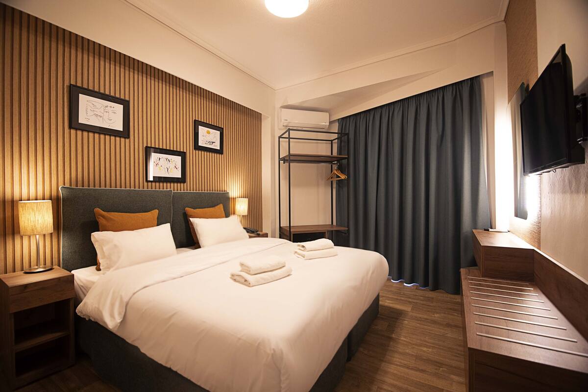 Une chambre d’hôtel avec un grand lit, des tables de chevet, un téléviseur fixé au mur et un porte-manteau.