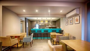 A modern dining area with a bar, multiple seating options, and a kitchen in the background. - Falireon Hotel (Palaio Faliro)