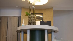 A reception desk with a green cylindrical base, white columns, and a patterned lamp above. - Falireon Hotel (Palaio Faliro)