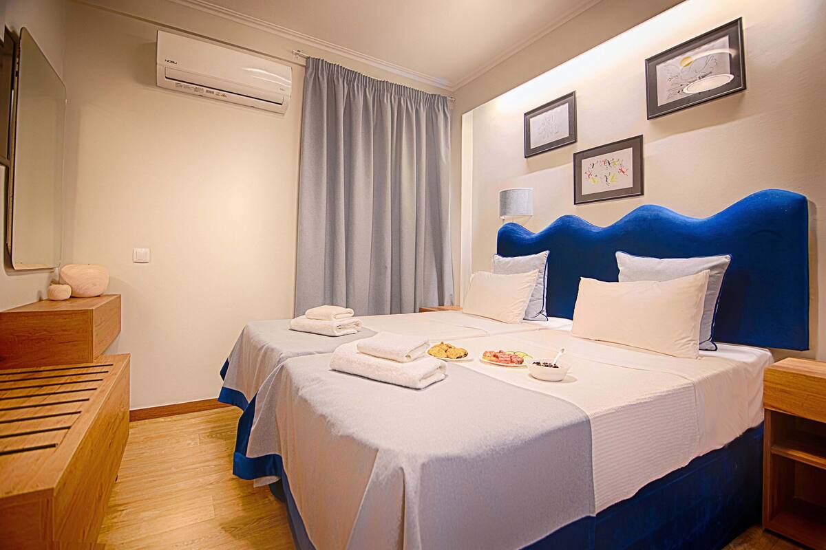 Une chambre d’hôtel avec deux lits, une commode en bois, un climatiseur et une fenêtre avec un rideau.