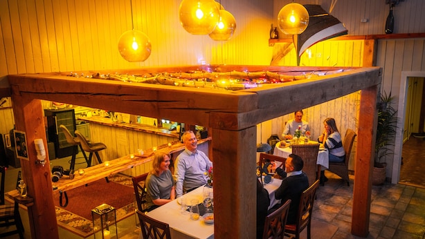 Un restaurante con mesas y sillas de madera, una zona de bar y lámparas colgantes.