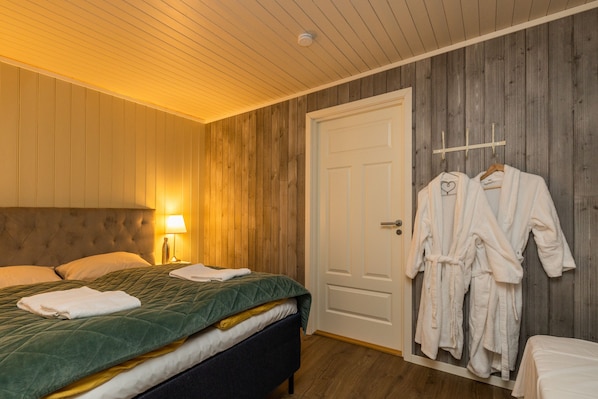 A bedroom with a bed, a bedside table with a lamp, and a door with two white robes hanging on a rack.