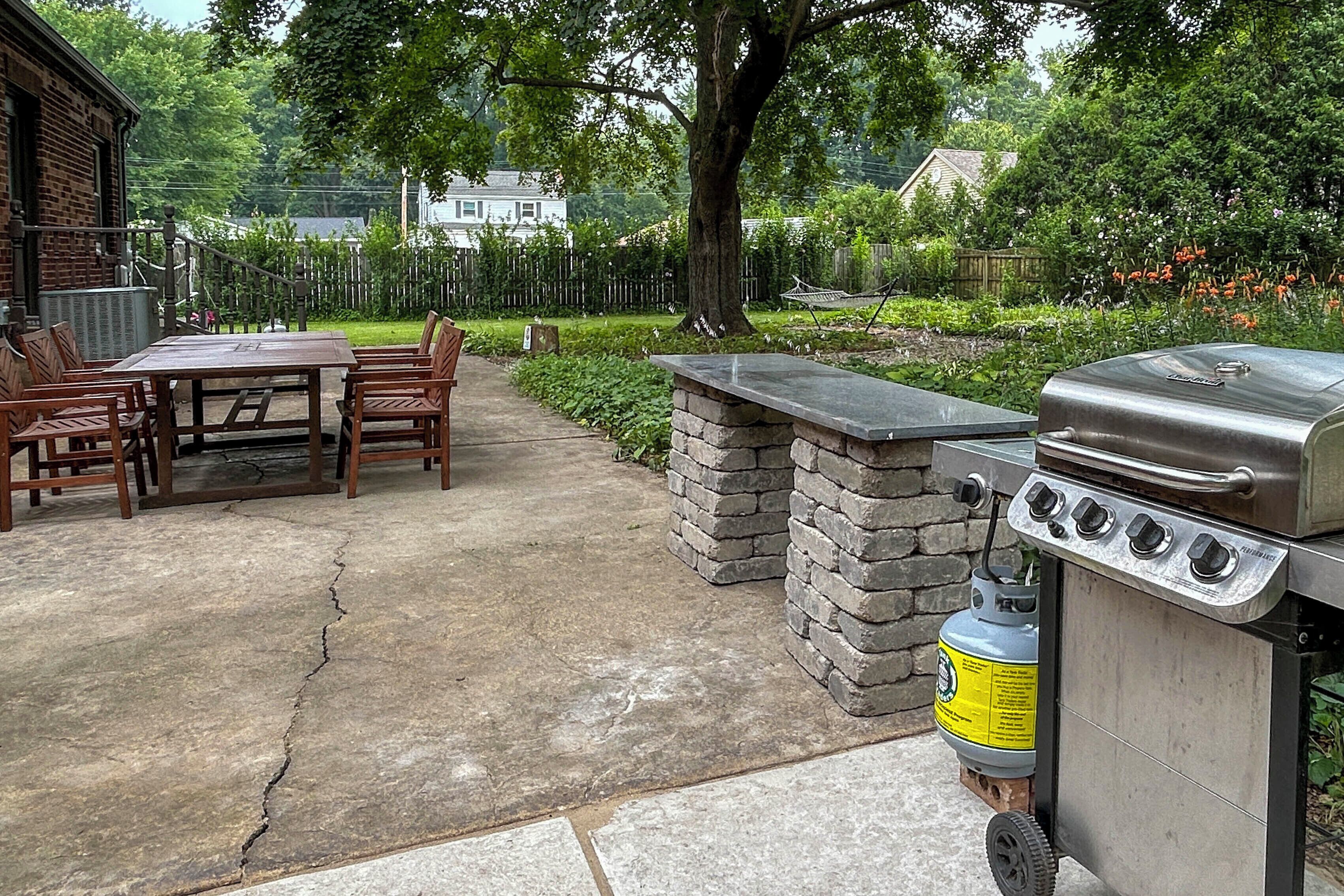 Un patio exterior con una parrilla, paredes de piedra y una zona de comedor con sillas.