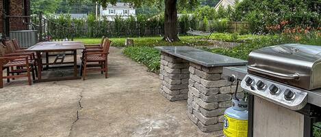 An outdoor patio with a grill, stone walls, and a dining area with chairs.