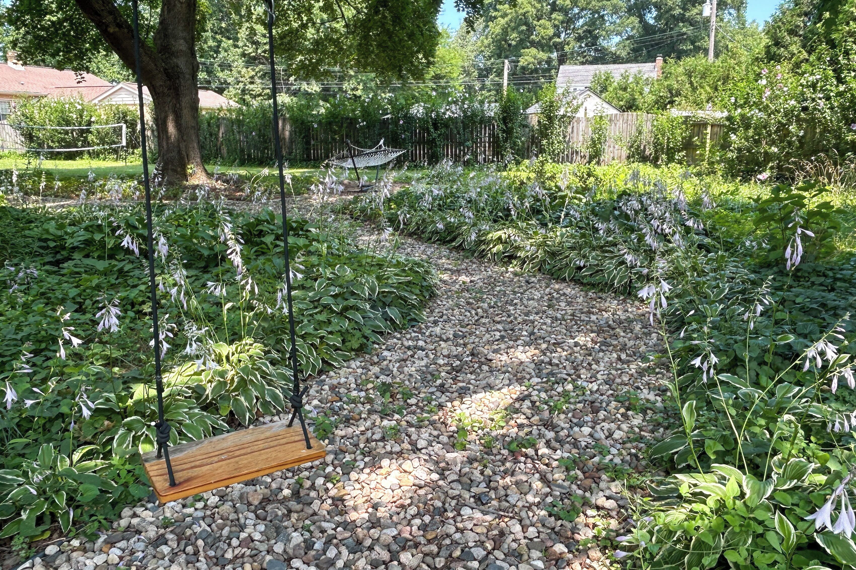A garden with a gravel path, a wooden swing, and various plants.