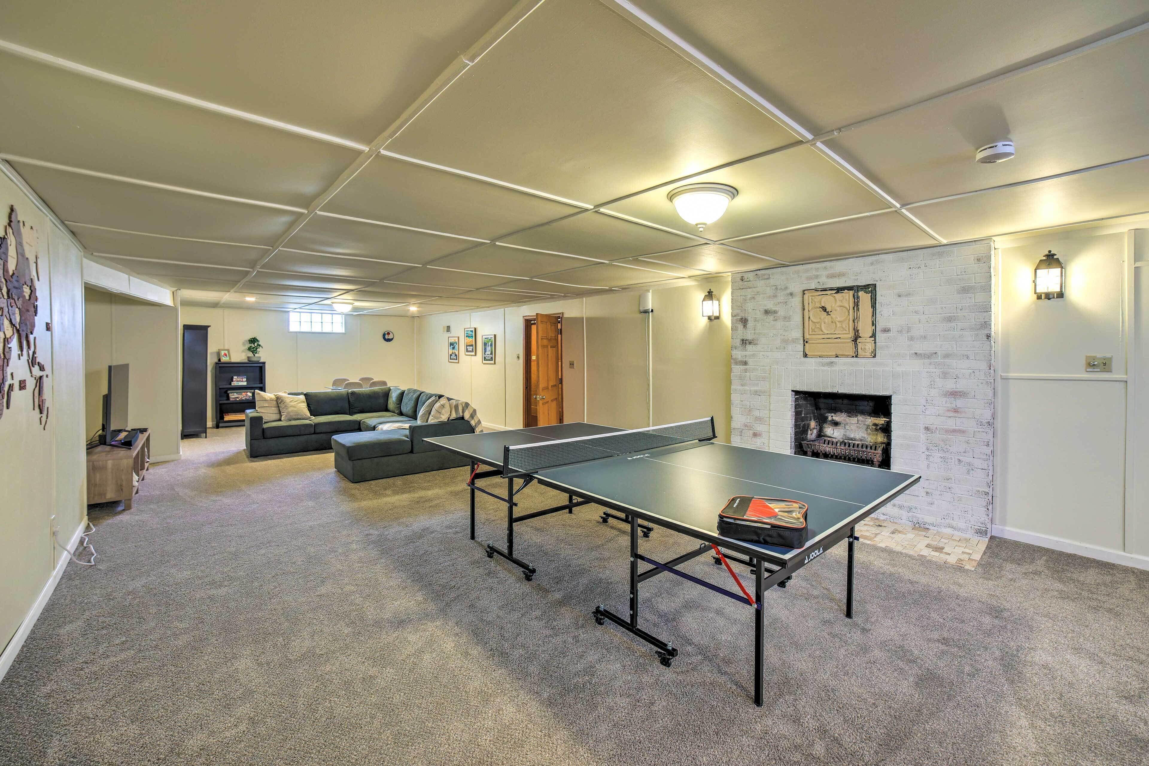 A room with a ping pong table, a couch, a fireplace, and a wall with pictures.