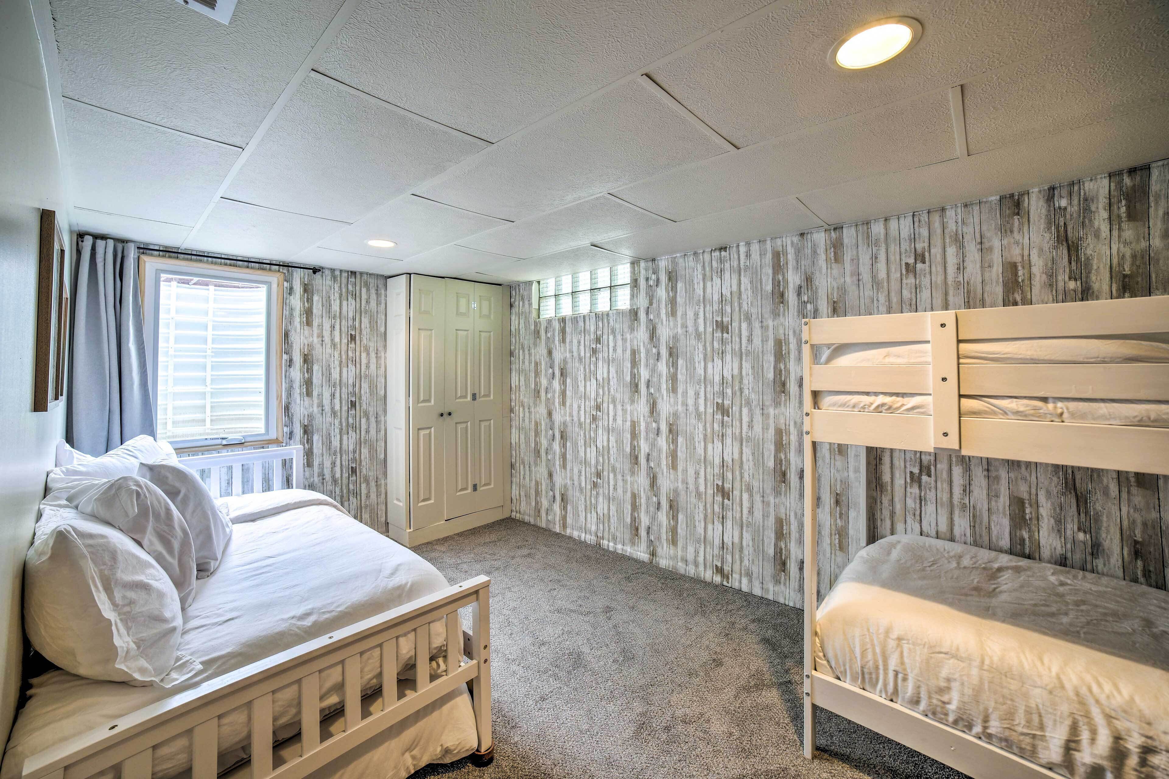 Une chambre avec un lit superposé, un lit simple, une fenêtre avec des rideaux, une armoire et un mur en bois.