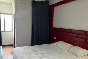 Ein Hotelzimmer mit Bett, rotem Kopfteil, einem Fenster mit Vorhängen und einer Tür.