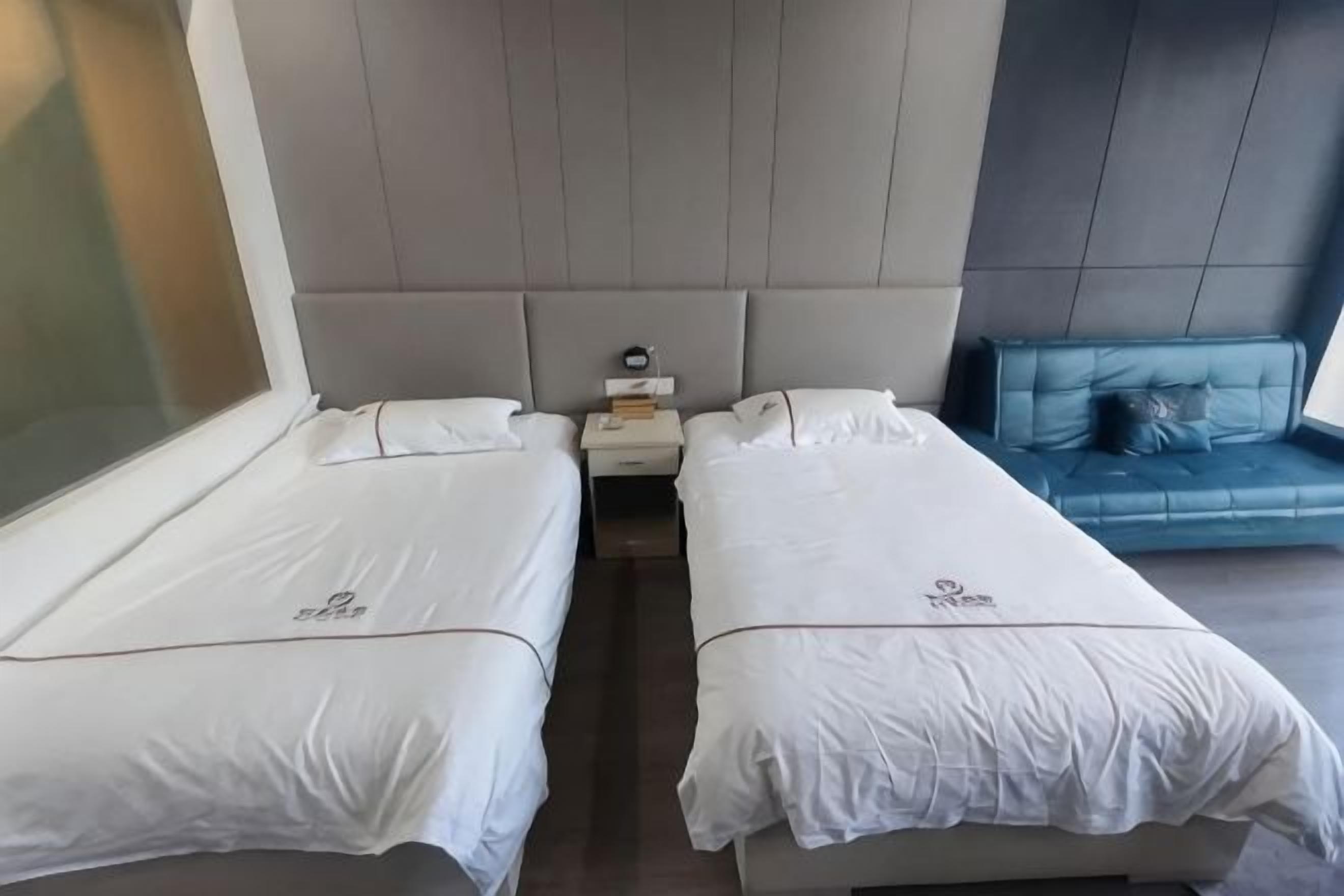 A hotel room with two single beds, a nightstand with a lamp, and a blue sofa.