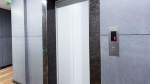 Ein Aufzug mit digitaler Anzeige, die die Zahl 1 zeigt, umgeben von grauen Wänden mit Marmoroptik.