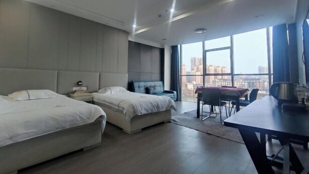 Ein modernes Hotelzimmer mit zwei Betten, einem Essbereich und großen Fenstern mit Blick auf die Stadt.