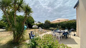 An outdoor patio area with a table and chairs, surrounded by plants and a palm tree. - Traditional house with garden and activities, quiet near the sea (La Baule)