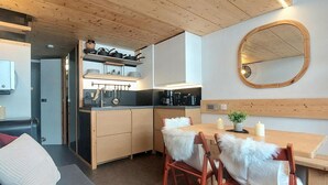 A compact kitchen with wooden cabinets, a dining area with a table and chairs, and a large mirror on the wall. - Mezzanine Duplex 5 pers. · Ski-in/out · Mont Blanc View (Les Arcs 1800)