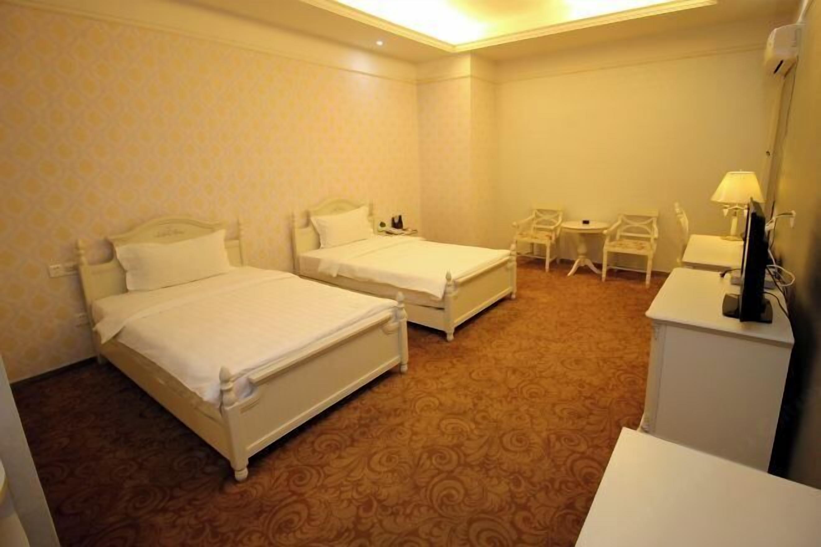 A hotel room with two beds, a desk, a chair, and a TV.