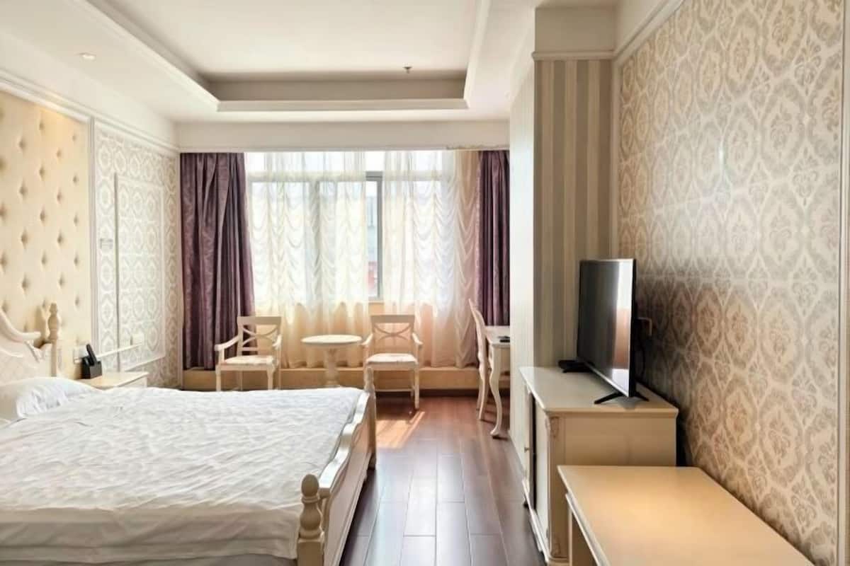 A hotel room with a bed, a TV, a desk, and a seating area with chairs and a table.