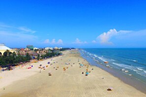 Una playa con una extensa franja de arena, algunos sombrillas y edificios al fondo.