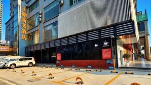 Un hotel con fachada moderna, un estacionamiento con espacios delimitados y un letrero que indica una cafetería.