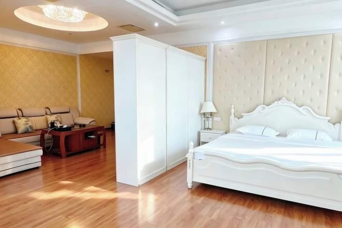 A bedroom with a bed, a wardrobe, a nightstand, a lamp, and a sofa.