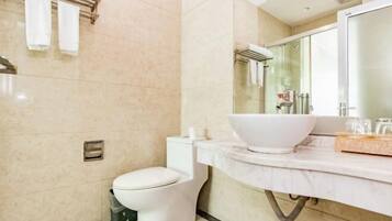 A modern bathroom with a toilet, a large white sink, and a glass shower enclosure.