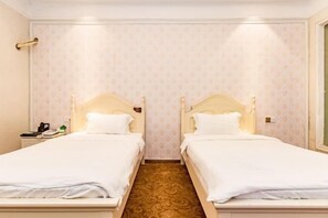 A hotel room with two single beds, a nightstand with a phone and a lamp, and a patterned carpet.