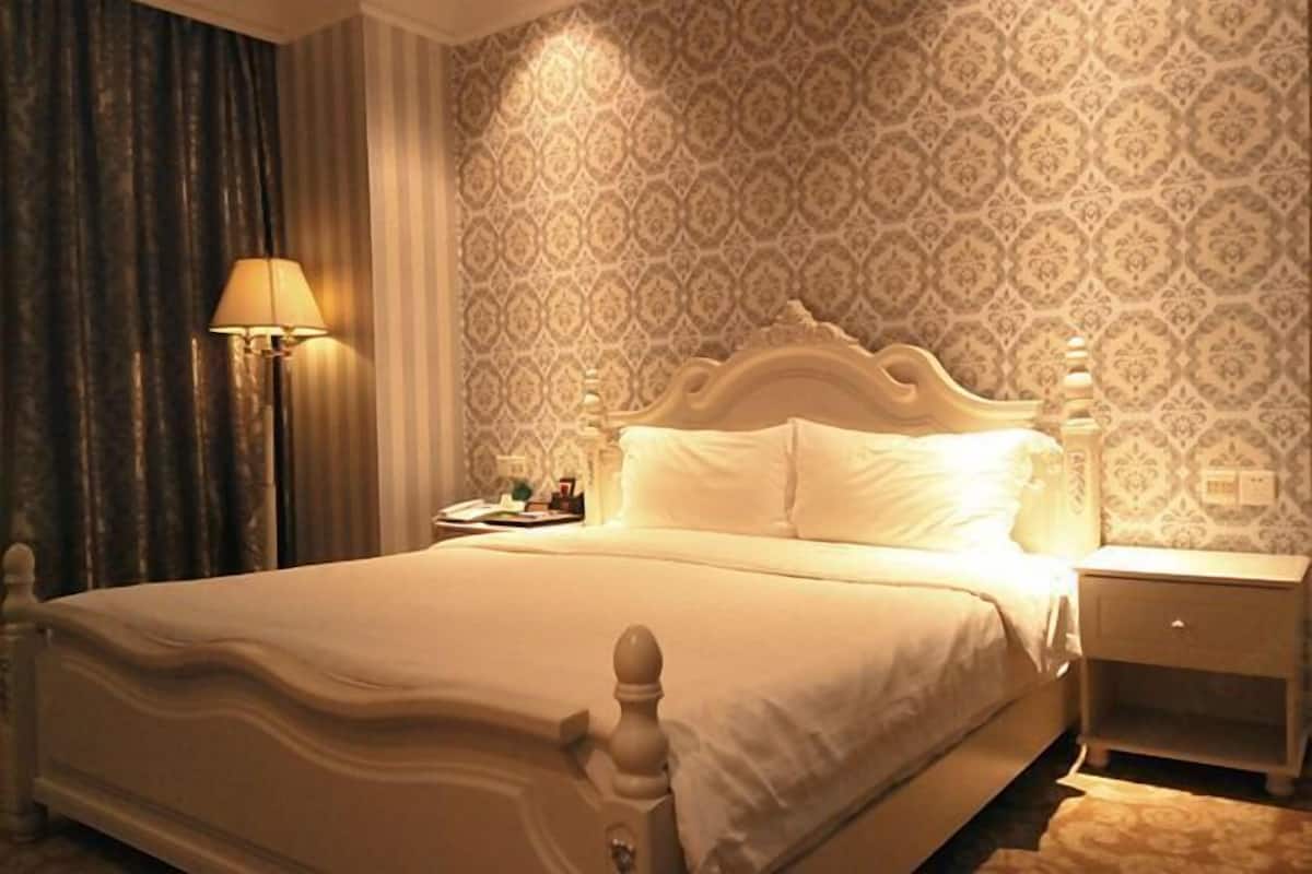 A hotel room with a large bed, a nightstand, a lamp, and patterned wallpaper.
