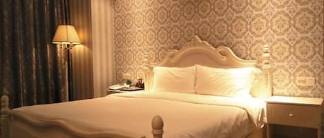 A hotel room with a large bed, a nightstand, a lamp, and patterned wallpaper.