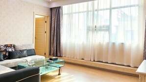 Una sala de estar moderna con una mesa de centro de vidrio, un sofá con cojines y un amplio ventanal con cortinas.