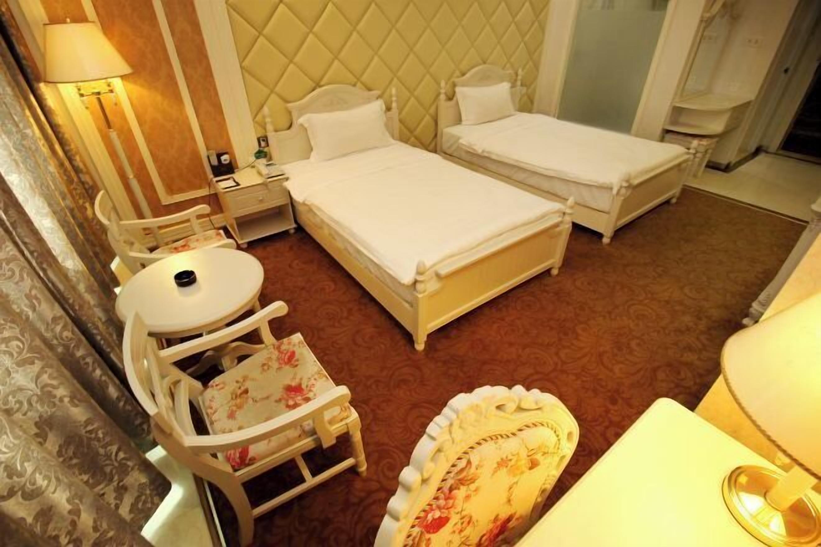 A hotel room with two beds, a small table, a chair, and a lamp.