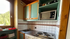 Cocina compacta con lavamanos, estufa y microondas. Cuenta con muebles de madera y un ventanal que proporciona luz natural.