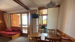 Una habitación acogedora con una cama de madera, una mesa de comedor con sillas, un televisor y una ventana con cortinas.