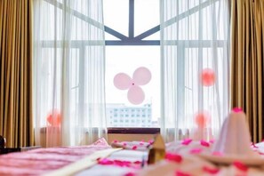 A hotel room with a large window, sheer curtains, and a view of the cityscape.