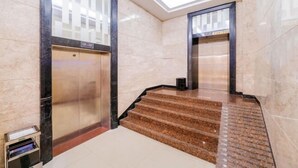 A modern elevator with a glass panel and a digital display, a marble staircase with a patterned carpet, and a clean, tiled floor. - Shenzhen Jiehao Business Hotel (Bao'an Airport Guyi Subway Station) (Shenzhen)