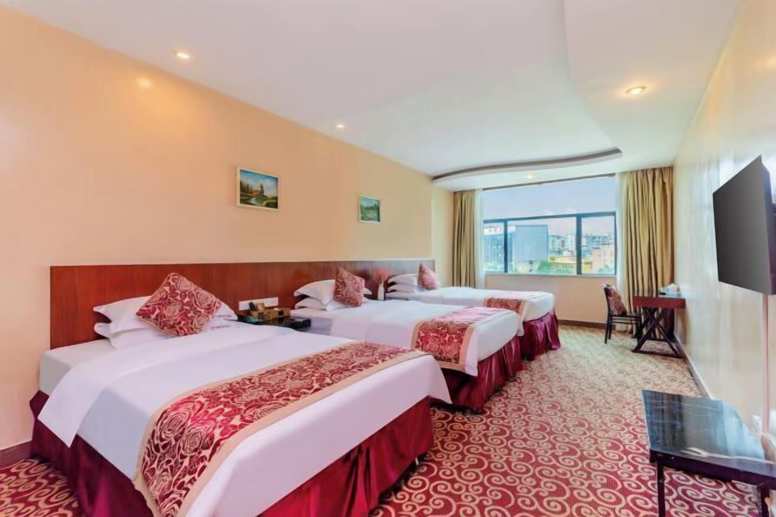 Habitación de hotel con dos camas, televisión, escritorio y vistas a la ciudad.