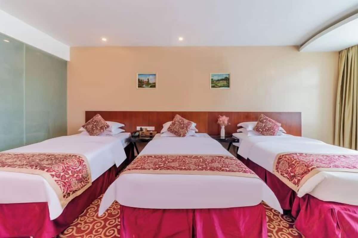 A hotel room with three beds, a wooden headboard, and two framed pictures on the wall.